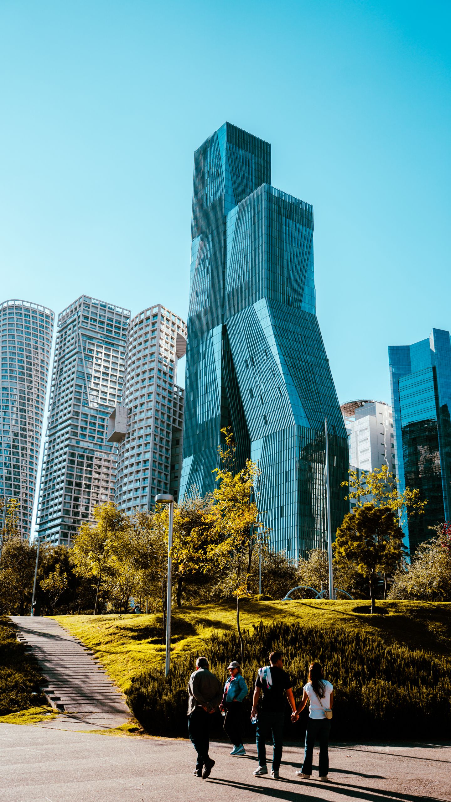 Dramatic cityscape with futuristic skyscrapers and a park under a clear blue sky.