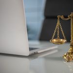 Golden justice scales on a desk beside a laptop, symbolizing law and balance.